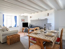 A living room with a dining table set for four a gray sofa a wicker basket a TV and a fireplace at Glan Y Mor Borth in Borth