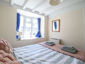 A bedroom with a bed with folded towels on a pink runner a window with blue curtains and a small lamp on the windowsill at Glan Y Mor Borth in Borth