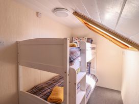 A small bedroom with white bunk beds under a slanted ceiling with a skylight at Glan Y Mor Borth in Borth