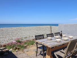 An outdoor wooden table set with bowls glasses and a bottle of wine on a stone patio overlooking a pebble beach and ocean at Glan Y Mor Borth in Borth