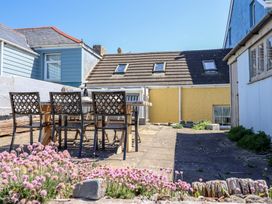 An outdoor patio area with a wooden table and chairs surrounded by buildings and pink flowers at Glan Y Mor Borth in Borth