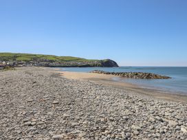 A pebble and sandy beach with a rocky jetty and houses and green hills in the background at Glan Y Mor Borth