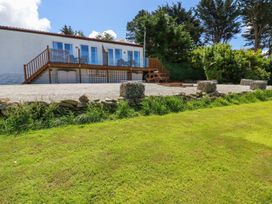 A white building with a wooden deck and glass railings overlooking a gravel area and green lawn at Meadows Edge Perranwell near Goonhavern