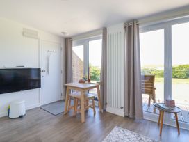 A room with a wall mounted tv a small dining table with stools large windows with curtains and a small side table at Meadows Edge in Perranwell near Goonhavern