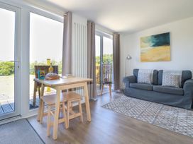 A living room with a sofa a small wooden dining table stools glass doors and a painting at Meadows Edge in Perranwell near Goonhavern