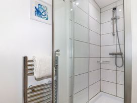 A bathroom shower area with a glass door and tiled walls with a detachable showerhead a towel rail with a white towel and a framed octopus picture on the wall at Meadows Edge in Perranwell near Goonhavern