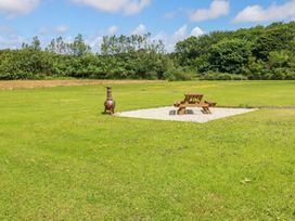 A picnic table and a chiminea on a gravel patch in an open grassy field with trees in the background at Meadows Edge in Perranwell near Goonhavern