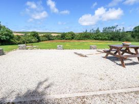 A gravel area with a wooden picnic table and a bowl on it overlooking a grassy field and trees at Meadows Edge in Perranwell near Goonhavern