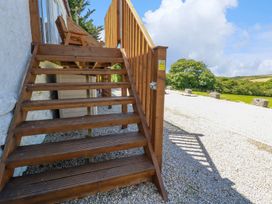Wooden outdoor stairs leading to a deck with a wooden railing and gravel ground at Meadows Edge in Perranwell near Goonhavern