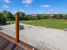 A gravel patio with a wooden picnic table and grass field with trees and hills in the background at Meadows Edge in Perranwell near Goonhavern