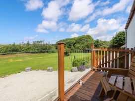A wooden balcony with chairs overlooking a green lawn and trees at Meadows Edge in Perranwell near Goonhavern