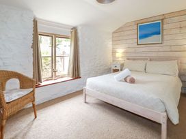 A bedroom with a bed a lamp on a nightstand a wicker chair and a window with curtains at Babes Cottage in Perranwell near Goonhavern