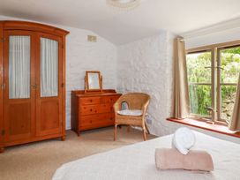 A bedroom with wooden wardrobe wooden dresser wicker chair and window with curtains at Babes Cottage in Perranwell near Goonhavern