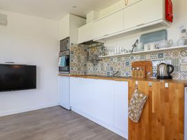 A kitchen with white cabinets wooden countertops patterned tile backsplash and a wall mounted TV at The Lookout in Perranwell near Goonhavern