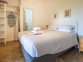 A bedroom with a bed with folded towels and pillows an open wardrobe with an ironing board and iron a bedside table and two framed pictures on the wall at The Lookout in Perranwell near Goonhavern