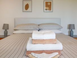 A bedroom with a bed with striped linens and stacked towels in the center with lamps and framed pictures on the wall at The Lookout in Perranwell near Goonhavern