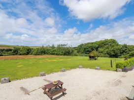 An outdoor area with a small wooden picnic table on gravel and a grassy field with a small thatched gazebo at The Lookout in Perranwell near Goonhavern