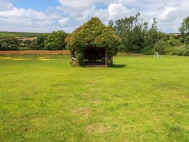 A grassy field with a small wooden shelter covered in vines and trees in the background at The Lookout in Perranwell near Goonhavern