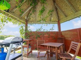 An outdoor covered seating area with a barbecue grill a small wooden table and three wooden chairs at The Lookout in Perranwell near Goonhavern