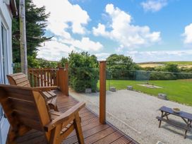 A wooden deck with two chairs and glass railing overlooking a gravel area and green field at The Lookout in Perranwell near Goonhavern