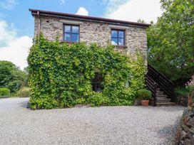 A stone cottage with ivy on the wall and outdoor stairs surrounded by greenery at Hollies Cottage in Perranwell near Goonhavern