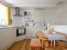 A kitchen with wooden floor cabinets a wooden table with bench seating and kitchen appliances at Hollies Cottage in Perranwell near Goonhavern