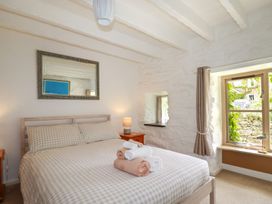 A bedroom with a double bed with folded towels a bedside table with a lamp and a window with curtains at Hollies Cottage in Perranwell near Goonhavern