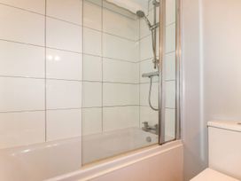 A bathroom with a bathtub shower combination and white tiled walls at Hollies Cottage in Perranwell near Goonhavern