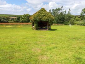 A grassy field with a small wooden shelter covered in greenery and a small white goal at Hollies Cottage in Perranwell near Goonhavern