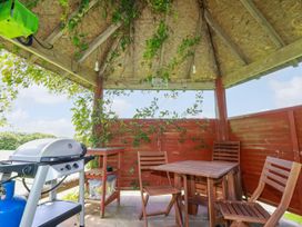 An outdoor gazebo with wooden chairs and table and a gas barbecue grill at Hollies Cottage in Perranwell near Goonhavern
