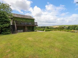 A grassy lawn with a stone building covered in ivy and a wooden deck at Hollies Cottage in Perranwell near Goonhavern
