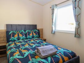 A bedroom with a bed with giraffe and palm tree bedding and a window with curtains at 4 Foxburrow Hang in Fritton near Belton Norfolk