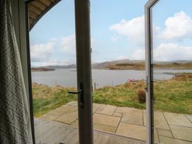 A view of a lake and hills through open glass doors with a stone patio and grass at Creags in Cullipool Isle Of Luing