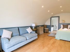 A room with a blue sofa, wooden chest of drawers, chair, bed with pillows, and an open doorway leading to a bathroom at Creags Cullipool Isle Of Luing