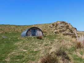 A small curved wooden cabin with glass doors set in a grassy hillside with a rocky outcrop nearby at Creags in Cullipool Isle Of Luing