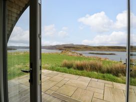 A patio door opening to a stone terrace with a grass lawn and water view at Erraid in South Cuan near Cullipool Isle Of Luing