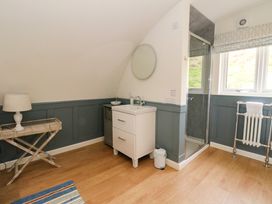 A bathroom with a white sink, round mirror, wooden floor, glass shower, towel rack, table with lamp and window at Erraid in South Cuan near Cullipool Isle Of Luing