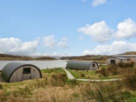 Two curved wooden cabins near a stone path by a body of water with hills in the background at Erraid South Cuan near Cullipool Isle Of Luing
