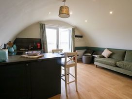 A living area with a kitchen counter, two white chairs, a green sofa, two round woven chairs, and double doors leading outside at Insh Cullipool Isle Of Luing