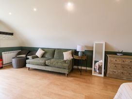 A sitting area with green sofa and cushions next to a lamp on a round table and a mirror beside a wooden dresser at Insh Cullipool Isle Of Luing