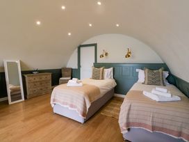 A bedroom with two single beds with beige blankets and pillows a wooden chest of drawers a wicker chair and a full-length mirror at Insh Cullipool Isle Of Luing