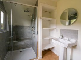 A bathroom with a shower enclosure a pedestal sink a round mirror and built-in shelving at Insh Cullipool Isle Of Luing