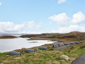 Small curved cabins on a grassy hillside near a body of water with hills in the background at Insh Cullipool Isle Of Luing