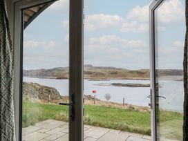A view through open glass doors showing a patio leading to grass and water with hills in the background at Sula in Cullipool Isle Of Luing