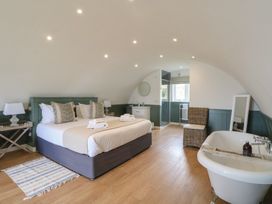 A bedroom with a bed side tables a chair a freestanding bathtub and a shower at Sula in Cullipool Isle Of Luing