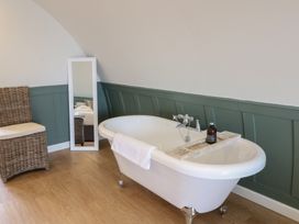 A bathroom with a freestanding bathtub a wicker chair and a floor mirror at Sula in Cullipool Isle Of Luing