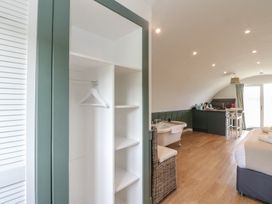 A room with an open closet with hangers a bathtub wicker chair a kitchenette and a bed at Sula Cullipool Isle Of Luing