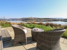 An outdoor patio with two wicker chairs and a table with two mugs overlooking a lake and grassy area at Sula Cullipool Isle Of Luing