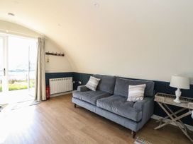 A living room with a gray sofa two pillows a wooden side table with a lamp a curtain a coat rack and a glass door at Scarba in Cullipool Isle Of Luing