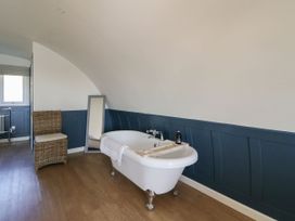 A bathroom with a freestanding bathtub a wicker chair and a floor mirror at Scarba in Cullipool Isle Of Luing